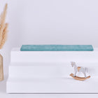 Ein weißer, dreistöckiger Ständer mit einem KraftKids GmbH Sitzauflage für Ikea TROFAST Cord Breitcord Mint Kissen auf der oberen Etage, einem kleinen weißen Holzschaukelpferd auf der unteren Etage und einer hohen Vase mit beigem Pampasgras auf der linken Seite, vor einem schlichten weißen Hintergrund.