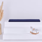 Ein weißes dreistufiges Podest mit einem KraftKids GmbH Sitzauflage für Ikea TROFAST Musselin dunkelblau Kissen auf der Oberseite, einem Schaukelpferd auf der untersten Stufe und einer hohen geflochtenen Vase mit Pampasgras auf der linken Seite, alles vor einem schlichten hellen Hintergrund.