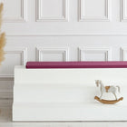 Ein minimalistisches Interieur mit einer hohen Vase mit Pampasgras, einer weißen Stufenbank mit der KraftKids GmbH Sitzauflage für Ikea TROFAST Leinen magenta dunkel und einem kleinen Holzschaukelpferd vor einer weiß getäfelten Wand.