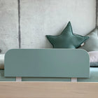 Ein minimalistisches Bett mit dem KraftKids Bettschutzgitter Rausfallschutz in blau petrolblau, gepaart mit mintgrünem Bettzeug und zwei sternförmigen Kissen vor einer Betonwand.