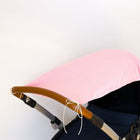 Auf einem dunkelnavyfarbenen Kinderwagen mit braunem Griff ist das KraftKids Sonnensegel "weiße Punkte auf Koralrosa" über das Verdeck drapiert, das auf einem schlichten weißen Hintergrund steht.