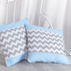 Zwei KraftKids Kissenbezüge - eines mit weißen Punkten auf hellblauem Grund, das andere in grauem Chevron - ruhen auf einem weißen Metallkopfteil. Die hellgraue Bettwäsche weist eine subtile Textur auf, die durch weiße Vorhänge im Hintergrund ergänzt wird.