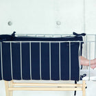 Eine Nahaufnahme eines Kinderbettes mit KraftKids Bettumrandung Nestchen Musselin dunkelblau, die nur die Füße eines Babys zwischen den Seitenstäben vor einer schlichten, hellen Wand zeigt.