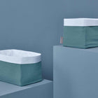 Zwei rechteckige KraftKids Körbchen Musselin-Stoffkörbe mit weißen Rändern und strukturierten tealfarbenen Seiten stehen auf blaugrauen Podesten vor einem passenden blaugrauen Hintergrund.