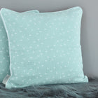 Zwei mintgrüne quadratische KraftKids Kissenbezüge Musselin Pusteblumen mit dezenten weißen Mustern ruhen vor einer grauen Wand auf einer flauschigen Oberfläche und verleihen Ihrer Bettwäschekollektion weichen Komfort und Stil.