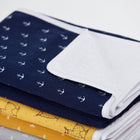 Eine Nahaufnahme von sauber gefalteten KraftKids-Babydecken, gekrönt von der Wickelunterlage Musselin dunkelblau Anker - marineblau mit weißen Ankern - auf gelb und weiß bedruckten Lagen, ideal zur Kombination mit einer wasserdichten Wickelunterlage.