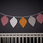 Die Wimpelkette Musselin senf grau rosa von KraftKids hängt über einem weißen Kinderbett an einer dunklen Wand - die perfekte Girlande fürs Kinderzimmer.