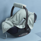 Eine schwarze Babyschale mit gepolstertem Griff wird von der KraftKids Babydecke für Babyschale Sommer Musselin mint vor hellblauen Wänden und Flächen bedeckt.