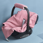 Eine schwarze Babyschale mit schwarzem Griff zeigt die rosa "Babydecke für Babyschale Sommer Musselin rosa" von KraftKids und ein Drei-Punkte-Gurt-System, platziert auf einer hellblauen Fläche vor einem passenden blauen Hintergrund.