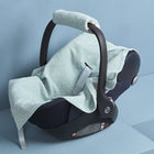 Eine Babydecke aus mintfarbenem Musselin mit Pusteblumenaufdruck von KraftKids, die für Autositze für Kleinkinder entworfen wurde, wird über einen Sitz drapiert und auf eine hellblaue Plattform vor einem passenden blauen Hintergrund gelegt.