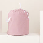 Der KraftKids Spielzeugkorb Musselin goldene Punkte auf Rosa hat kleine goldene Punkte, weiße Bandgriffe und einen Kordelzugverschluss - ideal als stilvolle Aufbewahrung Spielzeug im Kinderzimmer. Ausgestellt auf einem weißen Podest vor einem hellen Hintergrund.