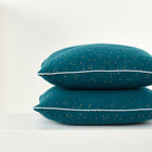 Zwei KraftKids Kissenbezüge Musselin mit goldenen Punkten auf Petrol und weißer Paspel liegen gestapelt auf weißem Untergrund - ein stilvolles Highlight für jede Bettwäschekollektion.