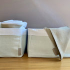 Zwei hellgrün-weiße KraftKids Körbchen Leinen sitzen auf einer hölzernen Oberfläche - perfekt für Wickeltisch Aufbewahrung, eine hält gefaltete Leinen und die andere hat ein beiges Tuch über den Rand drapiert. Beide sind mit einem kleinen KraftKids-Etikett versehen.