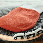 Ein KraftKids Strampelsack Herbst Winter Doppelkrepp Rot Herbstrot Schlafsack in Orange und Weiß ruht auf grauem Kunstfell, mit einer hölzernen Spielzeugeisenbahnschiene und einem weißen Zug im Vordergrund.