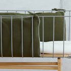 Eine Nahaufnahme eines modernen Babybettes mit grauem Metallrahmen, KraftKids Bettumrandung Nestchen Doppelkrepp Grün Herbstgrün an den Seiten, einer weißen Matratze und einem hellen Holzsockel vor einem neutralen Hintergrund.