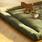 Eine KraftKids Krabbeldecke Doppelkrepp Grün Herbstgrün ruht auf einem Holzboden, auf dem ein Spielzeugpferd auf Rädern und Klötze stehen. Das einfallende Sonnenlicht bringt die weich gepolsterte Polyestervlies-Spieldecke zum Leuchten und schafft eine warme, gemütliche Atmosphäre.