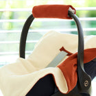 Eine Nahaufnahme einer KraftKids Decke für Babyschale Winter Doppelkrepp Rot Herbstrot mit Gurtöffnungen, die auf einem Babyautositz in einem Innenraum in der Nähe eines Fensters ausgestellt ist. Das Sonnenlicht durch die Jalousien schafft eine warme und gemütliche Atmosphäre.