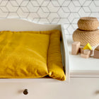 Ein weißer Wickeltisch mit einer KraftKids Wickelauflage Cord Breitcord Gelb Senf steht neben geflochtenen Körben und Holzklötzen vor einer weißen Wand mit einem schwarzen sechseckigen Fliesenmuster.