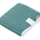 Die KraftKids Reisewickelunterlage Musselin nilblau ist eine sauber gefaltete, tealfarbene Musselin-Wickelunterlage mit weißem Rand und beigem SandDune-Anhänger - perfekt als platzsparende Wickelauflage oder Reise-Wickelunterlage für Eltern unterwegs.