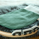 Ein KraftKids Strampelsack Frühling Sommer Doppelkrepp Grün Jade liegt auf einem grauen Kunstfellteppich neben einer hölzernen Spielzeugeisenbahnstrecke mit einem weißen Zug.