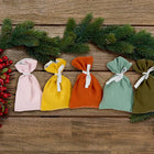 Fünf handgefertigte Stoffsäckchen von KraftKids aus der Reihe "Adventskalender Doppelkrepp Herbstgrün Gelb Rosa Weiß" sind auf Holz arrangiert - perfekt als wiederverwendbarer Adventskalender, dekoriert mit Tannenzweigen und Beeren.