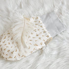 Der KraftKids Strampelsack Frühling Sommer Musselin Zweige braun besteht aus einem weichen, gemusterten Handschuh mit hellgrauem Bündchen und kleinen goldenen Zweigmustern, die auf einer weißen, flauschigen Oberfläche neben einer zarten weißen Feder zu sehen sind.